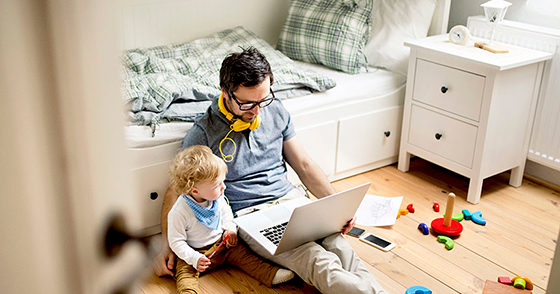 Man and son sitting on a bedroom floor and looking at a laptop screen together