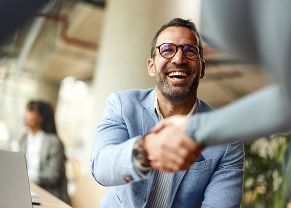 A smiling man in business attire shakes a persons hand.