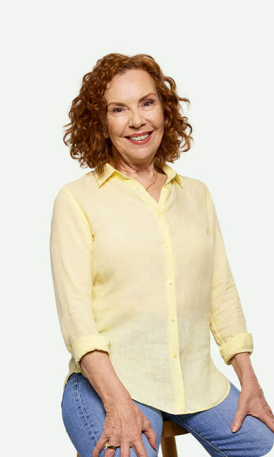 Mature woman, with curly red hair,  wearing a yellow shirt and smiling
