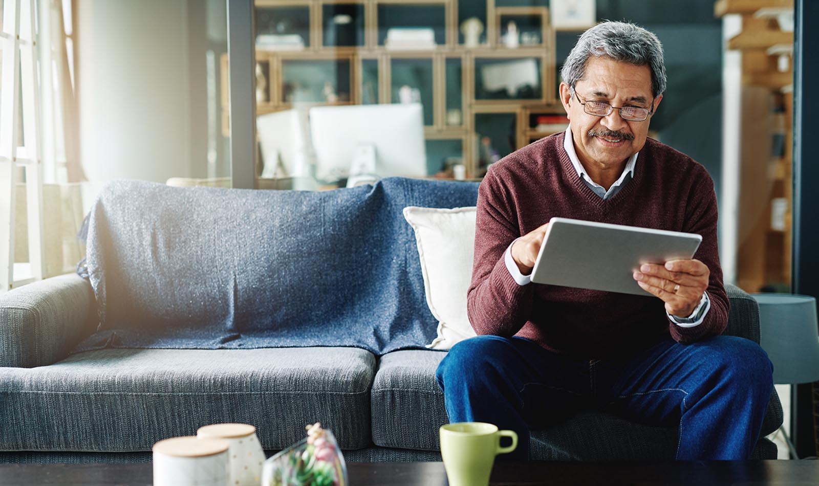 A man looks at information on a tablet device while sitting on a couch in a living room