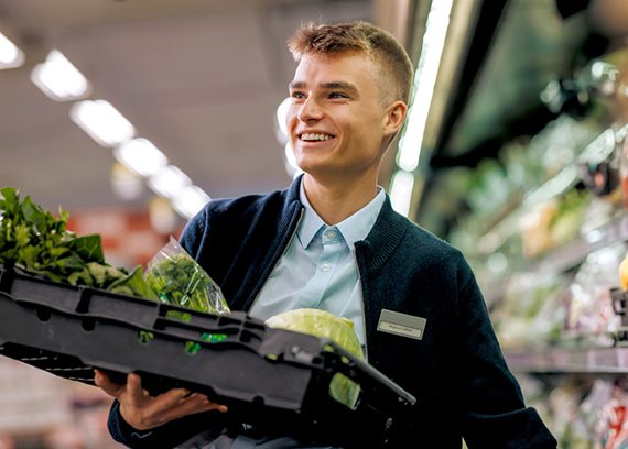 Supermarket worker holding a tray of fresh vegetables