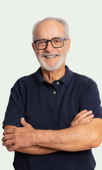 A mature man smiling. He has white facial hair, is wearing glasses and a dark blue polo shirt