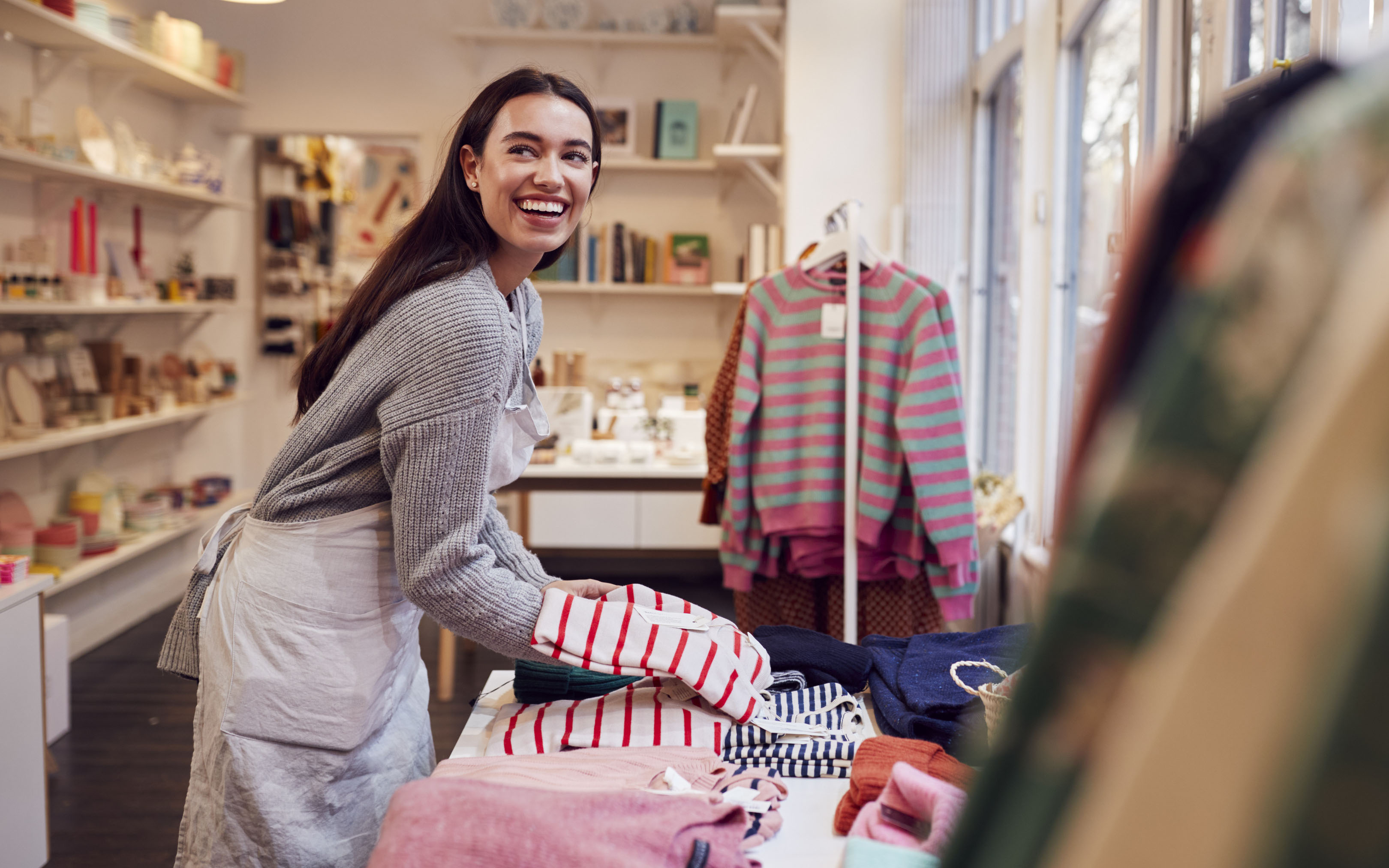 Smiling woman folding clothing items in a clothing store