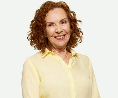 Mature woman, with curly red hair,  wearing a yellow shirt and smiling